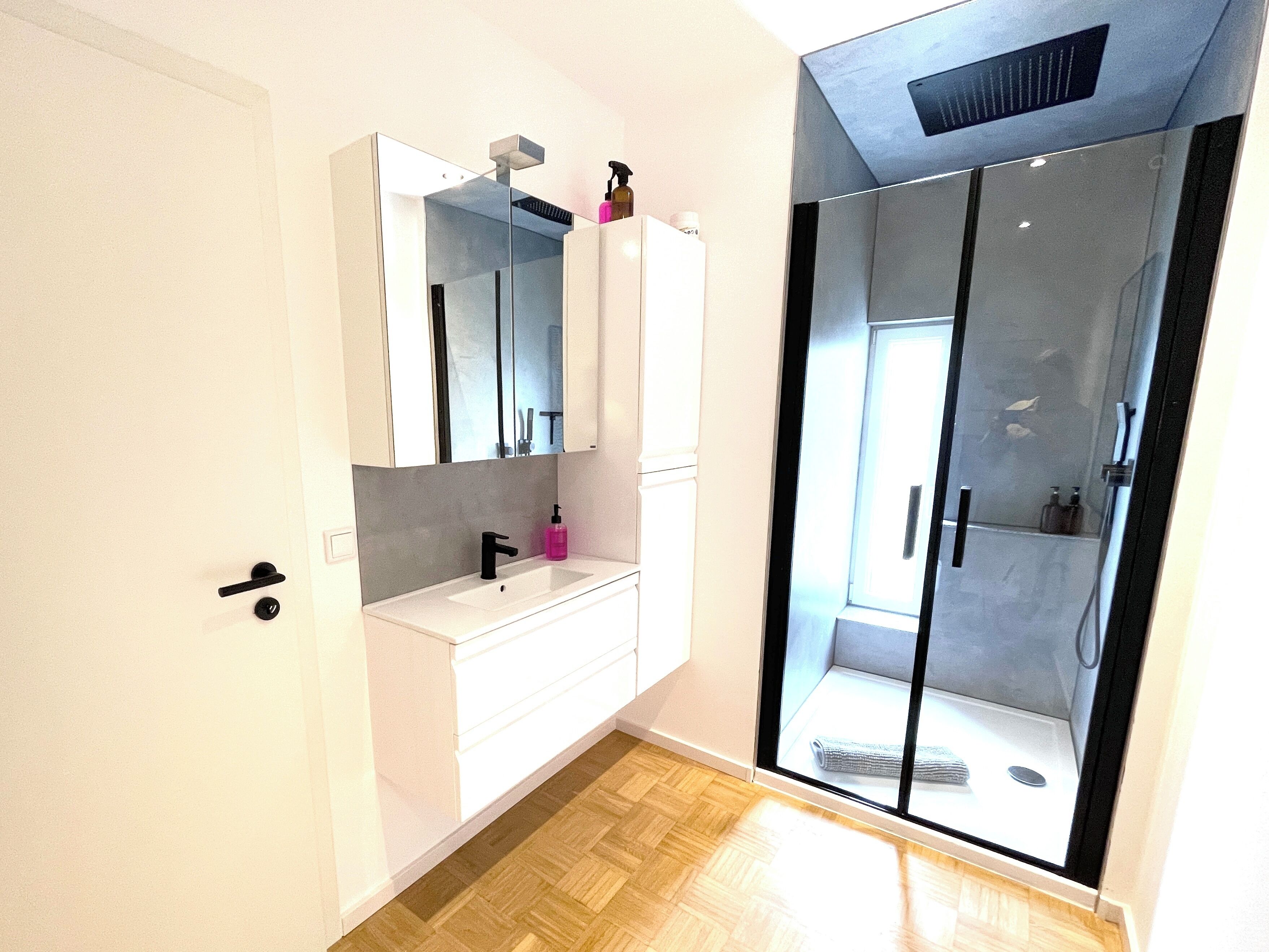 Un baño moderno con tocador blanco, un espejo grande y cabina de ducha con mampara de vidrio.