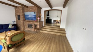 Ein Wohnzimmer mit Kamin aus Ziegelsteinen, einem darüber hängenden Fernseher, einem Essbereich mit Tisch und Stühlen und einer Treppe, die in einen anderen Raum führt.