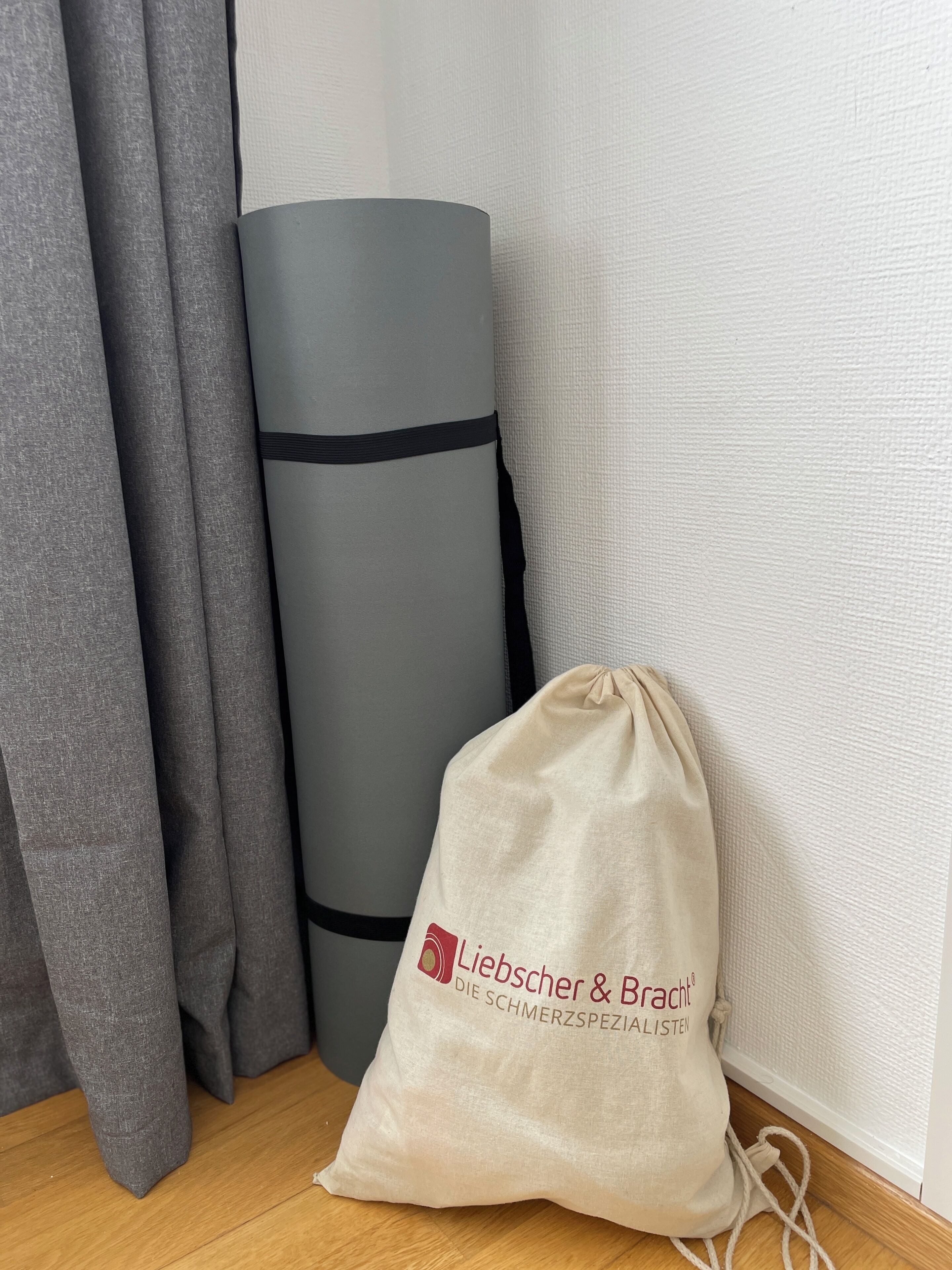 Une pièce avec un rideau gris, un tapis gris enroulé et un sac beige à cordon avec du texte.