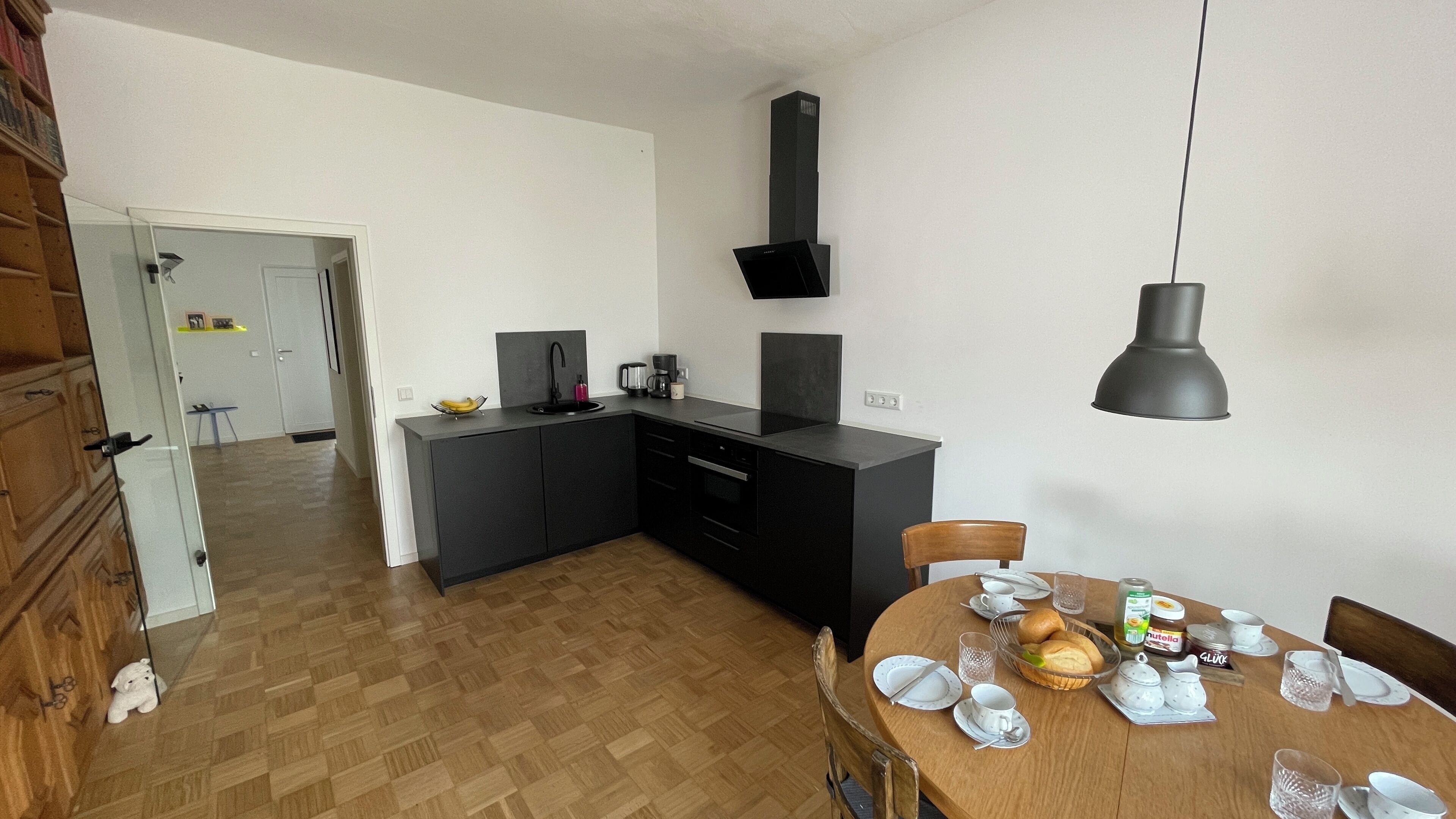 Una cocina moderna con armarios negros, horno empotrado y comedor con mesa de madera para cuatro.