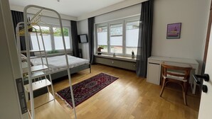 Ein Zimmer mit Etagenbett, Schreibtisch, Stuhl, Heizkörper und einem Fenster mit Vorhängen.
