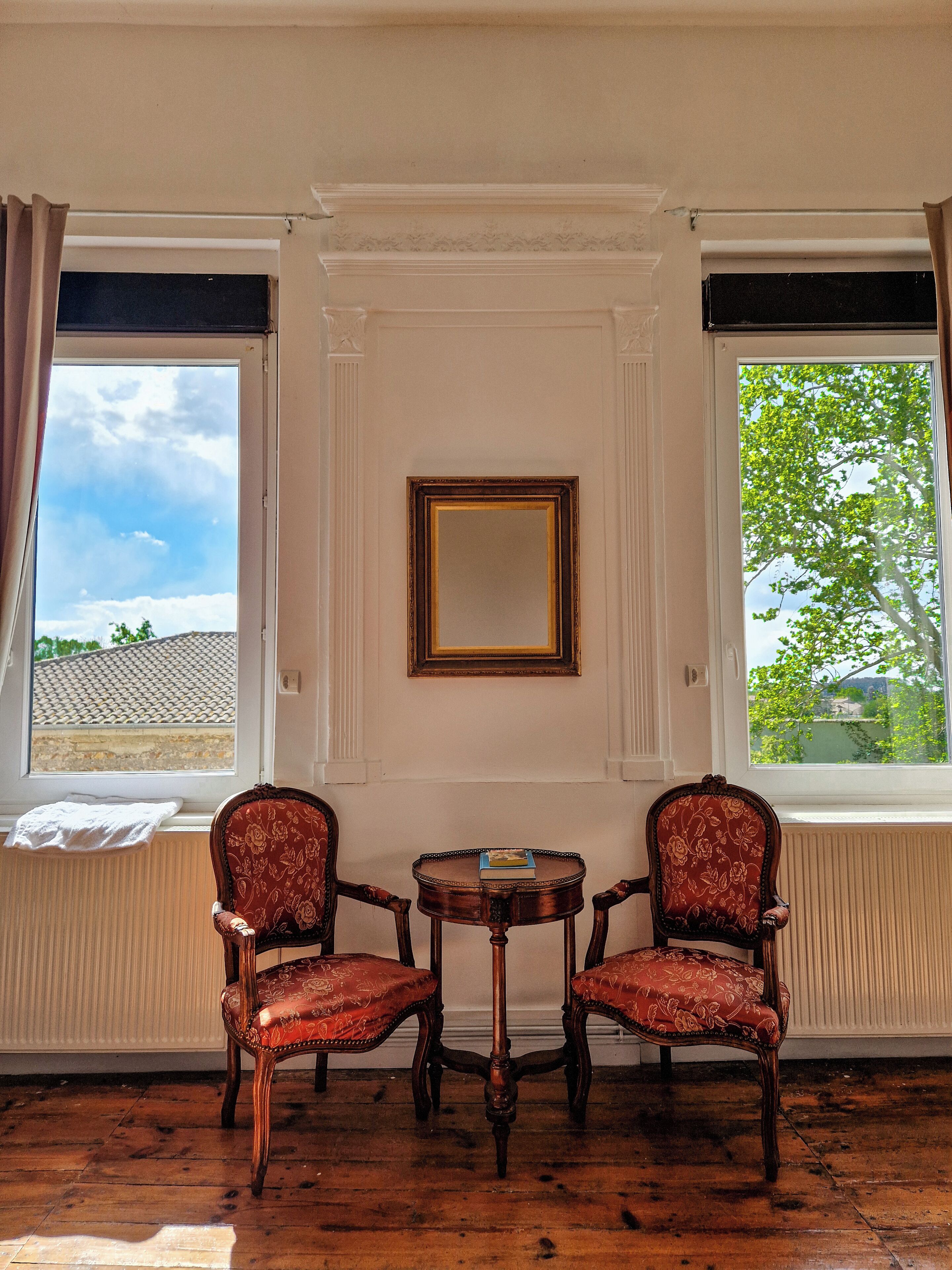 A room with two ornate chairs, a small table, and a mirror on the wall.