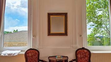 A room with two ornate chairs, a small table, and a mirror on the wall.