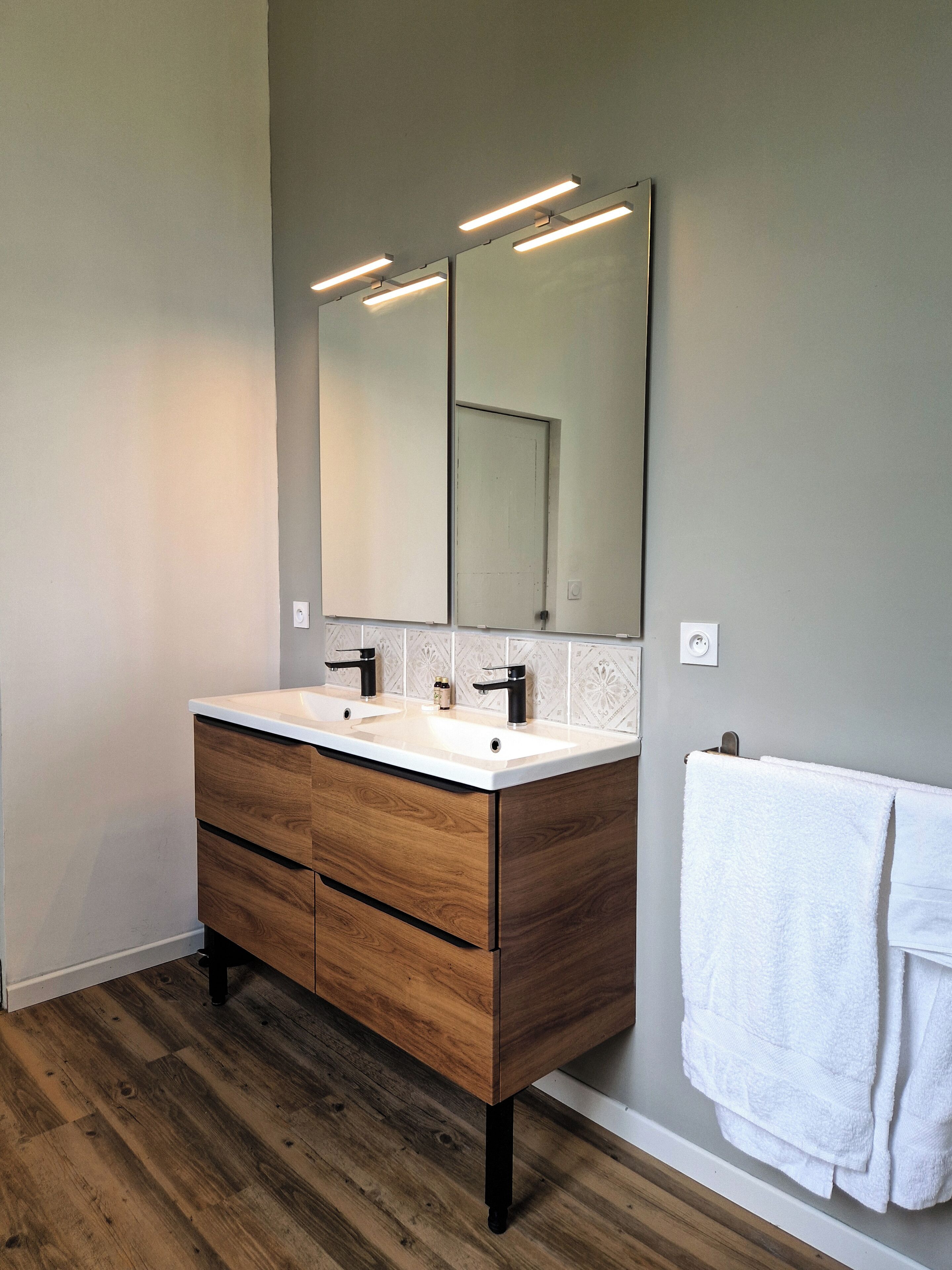 Un baño moderno con tocador de madera, dos lavamanos y un espejo grande.