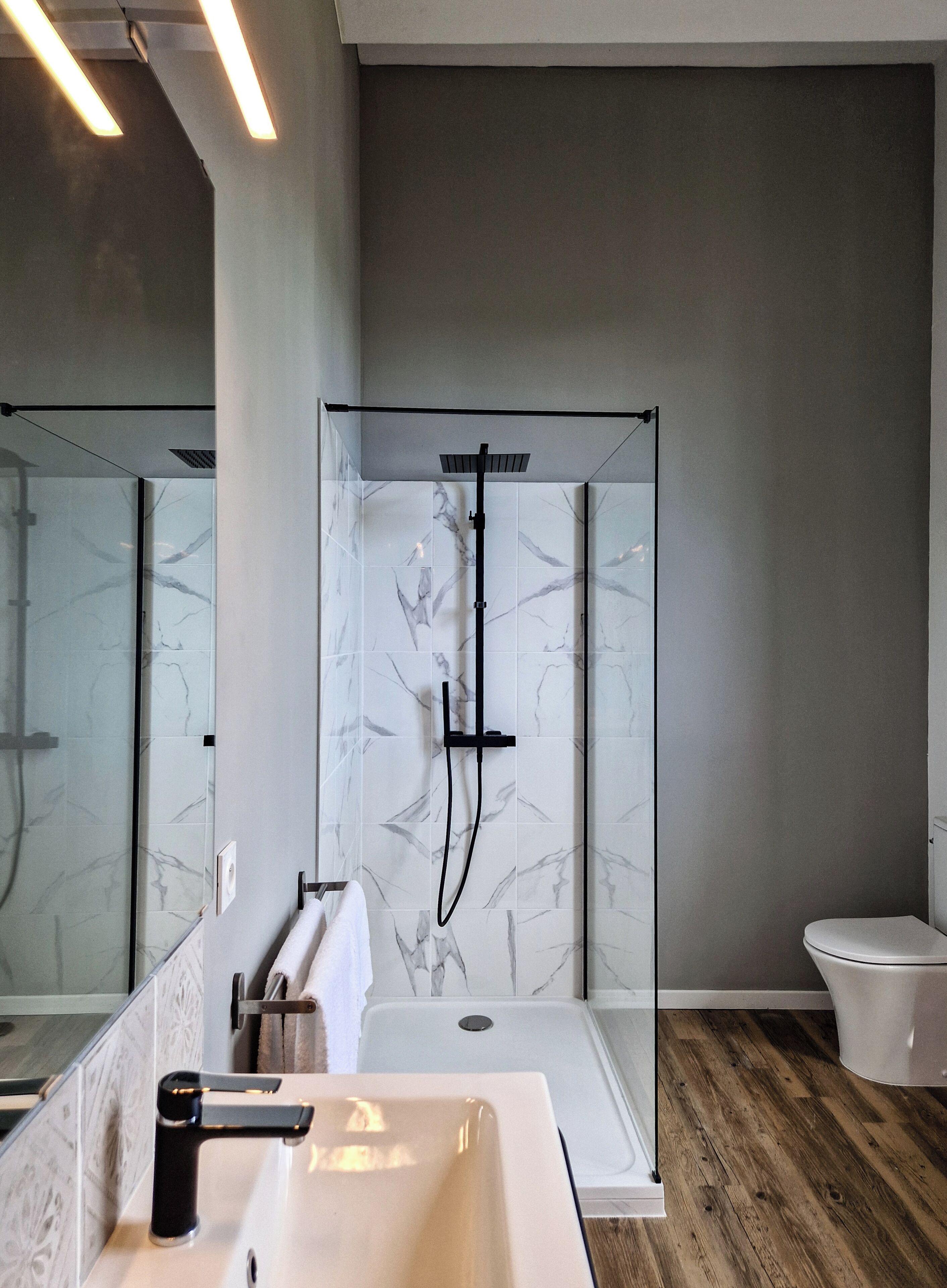 A modern bathroom with a large mirror, a white sink, a shower enclosure, and a toilet.