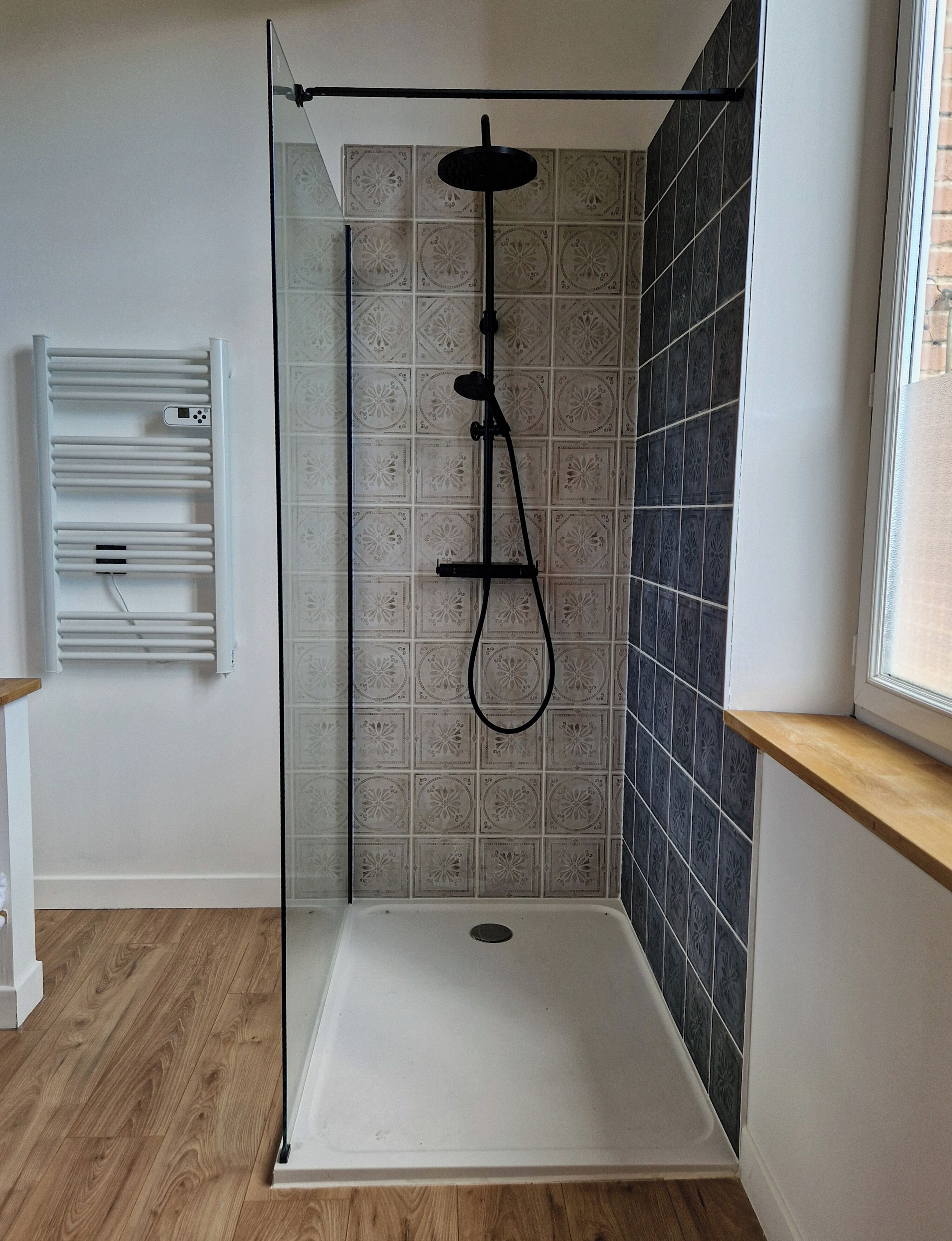 Una ducha con cerramiento de vidrio, pared de azulejos blancos y suelo de madera.