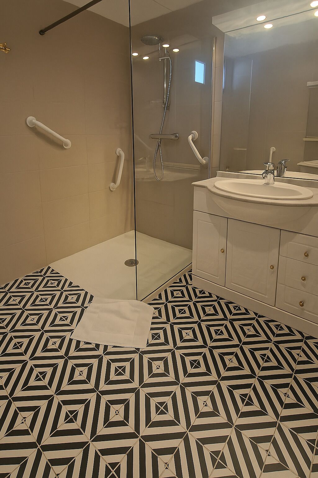 A modern bathroom with a glass shower enclosure, a white sink, and patterned floor tiles.