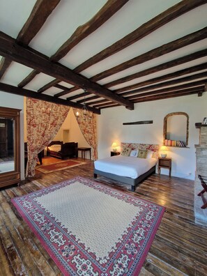 Une chambre avec un grand lit, des poutres en bois, un miroir et une petite table avec des livres.
