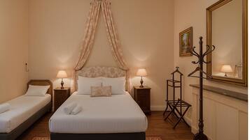 Habitación de hotel con una cama grande, dos camas más pequeñas, un espejo, un perchero y una mesita de noche con lámparas.