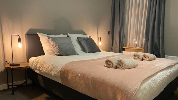 A neatly made bed with a beige blanket and two rolled towels, a bedside lamp, and a nightstand. - Hotel Restaurant 't Ronde Loegh (Winschoten)