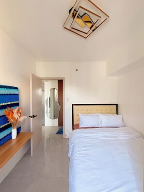 A hotel room with a bed, a mirror, a blue patterned sofa, and a decorative vase.