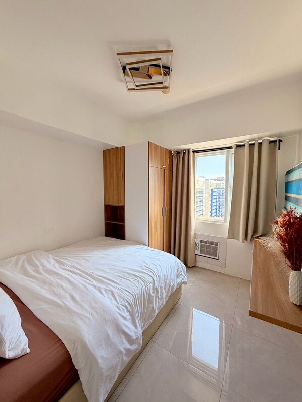 Habitación de hotel con cama, armario, tocador con espejo y ventana con cortinas.