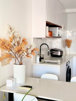 A modern kitchen with a white countertop, a sink, a microwave, and a toaster. There is a vase with dried flowers on the counter.
