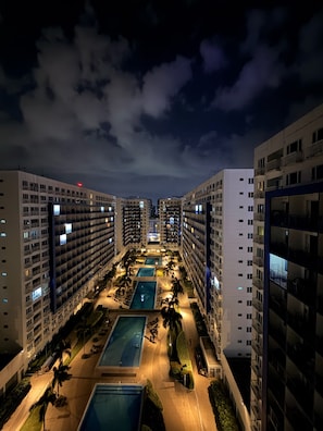 A high-rise hotel with multiple balconies, a central swimming pool, and a well-lit outdoor area.
