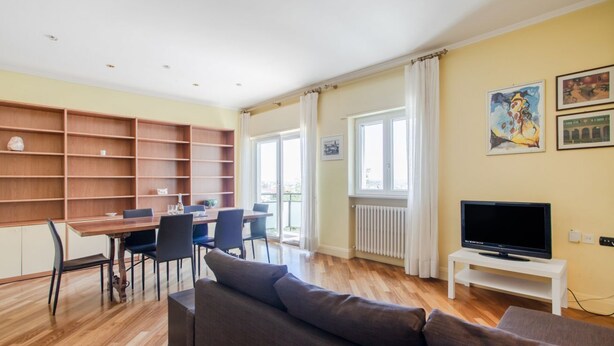 A living room with a sofa, a dining table with chairs, a TV on a stand, and a bookshelf. - Al Castello Apartment (Matera)