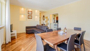 A modern living room with a wooden dining table, grey sofa, and a kitchen in the background. - Al Castello Apartment (Matera)
