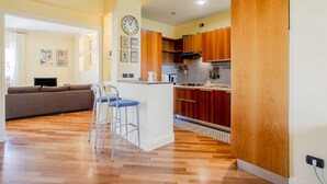 A modern kitchen with wooden cabinets, a central island, and a dining area with a sofa and bar stools. - Al Castello Apartment (Matera)