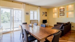 A dining area with a wooden table and chairs, a sofa, and a TV on a stand. - Al Castello Apartment (Matera)