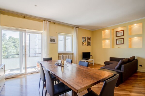 A dining area with a wooden table and chairs, a sofa, and a TV on a stand.