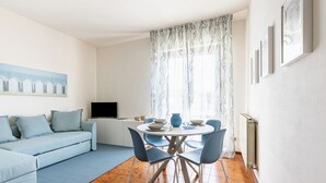 A modern living room with a sofa, dining table, chairs, a TV, and a window with curtains.