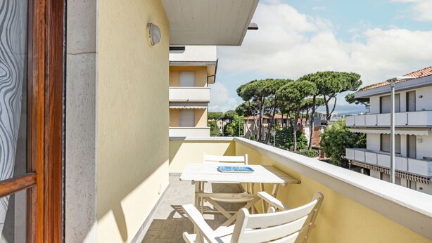 A balcony with a table and chairs, overlooking a residential area with trees and buildings.