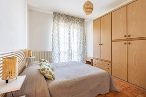 Quarto com cama, mesa de cabeceira, luminária, guarda-roupa e cortinas estampadas.
