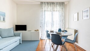 A living room with a sofa, a TV, a dining table with chairs, and a patterned curtain.