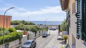 Een smalle straat met geparkeerde auto's, een gebouw met balkon en uitzicht op zee.