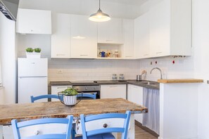 A modern kitchen with white cabinets, a wooden table, blue chairs, and a hanging light fixture.