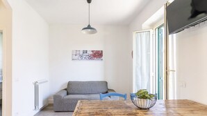 Een eethoek met een tafel, stoelen, een radiator, een foto aan de muur en een aan de wand bevestigde televisie.