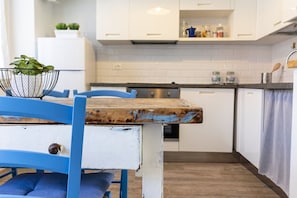 Una cocina con armarios blancos, una mesa de madera y una silla azul.