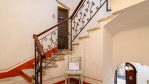 Una escalera con barandillas metálicas decoradas, una silla de madera y un piso a cuadros.