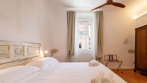 Habitación de hotel con una cama grande, un ventilador de techo de madera, vistas a través de una ventana con cortinas y un armario de madera.
