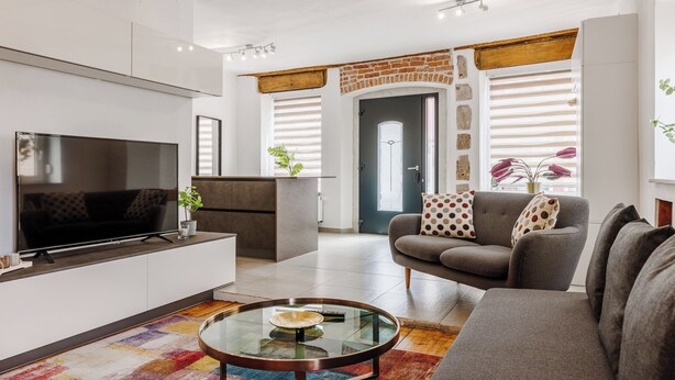 Una sala de estar moderna con un televisor de pantalla plana, una mesa de centro de vidrio, un sofá gris y una alfombra colorida.