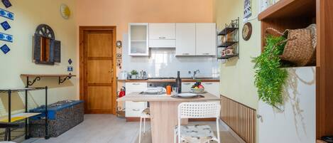 Una cocina compacta con armarios blancos, una puerta de madera y un comedor con una silla blanca y una mesa pequeña.