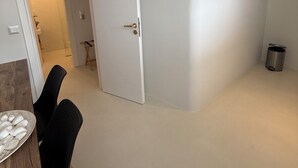 Ein Zimmer mit einer weißen Tür, einem kleinen Mülleimer und einem Essbereich mit Stühlen und einem Tisch.