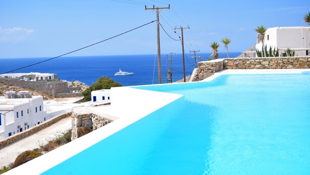 Ein klares, blaues Schwimmbecken mit Blick auf das Meer und weiße Gebäude.