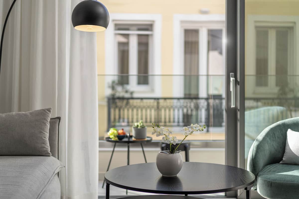 A modern living room with a sofa, a round table with a vase of flowers, and a view of the outside balcony.