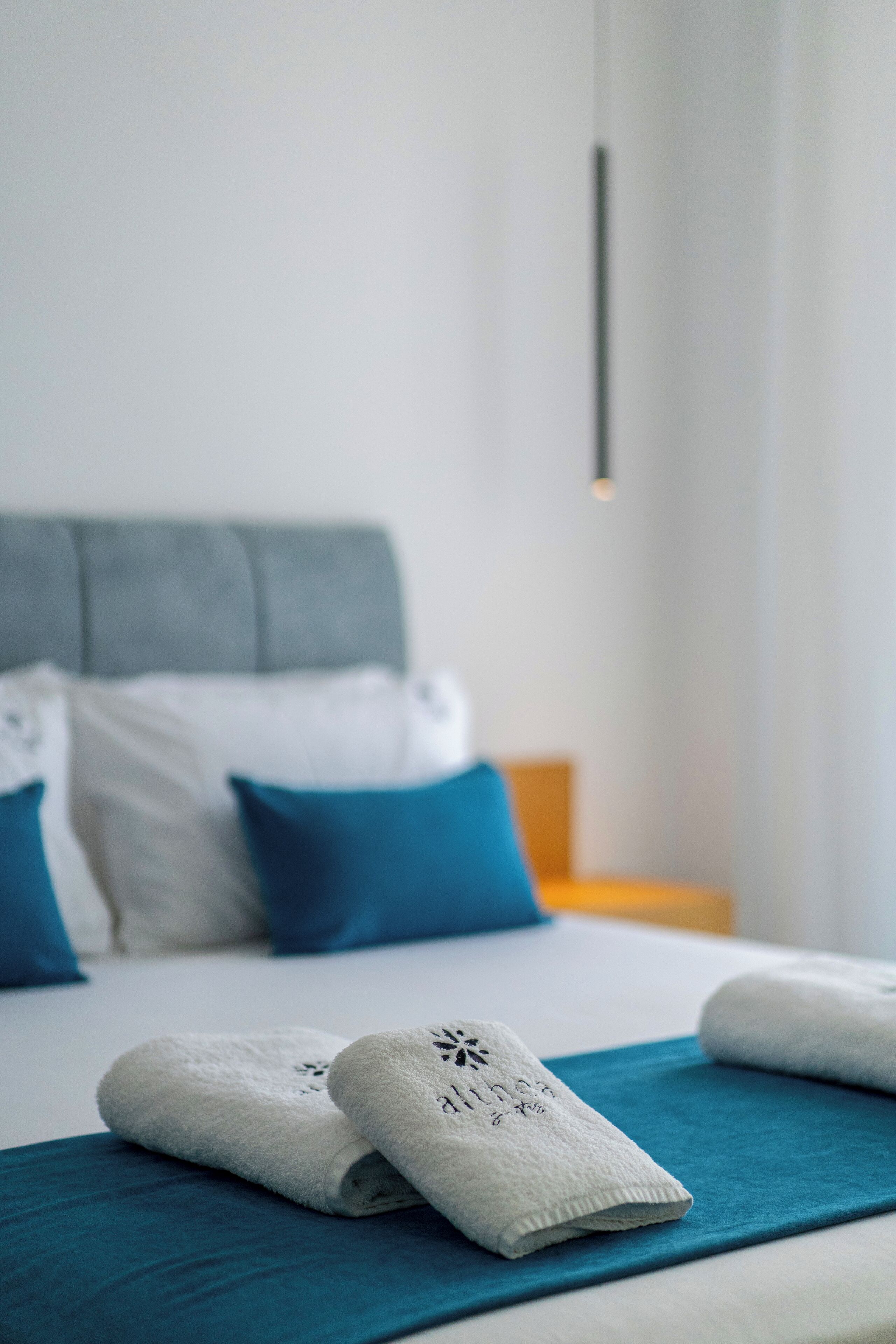 A neatly made bed with white and blue bedding, a grey headboard, and a teal throw blanket.