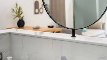 Un baño moderno con un lavamanos blanco, un espejo circular negro y un salpicadero de mármol.