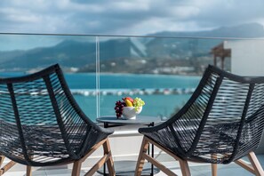 A balcony with two black wicker chairs and a table with a bowl of fruit. - Althea Suites (Sitia)