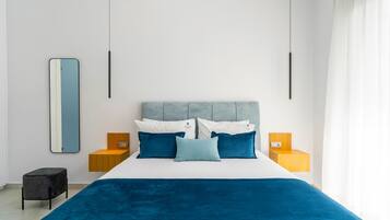 A modern bedroom with a large bed, a headboard, two bedside tables, a nightstand, a mirror, and a small stool.