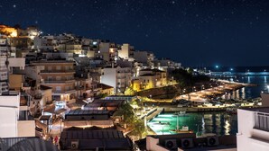 A coastal town at night with buildings, a marina, and a starry sky. - Althea Suites (Sitia)