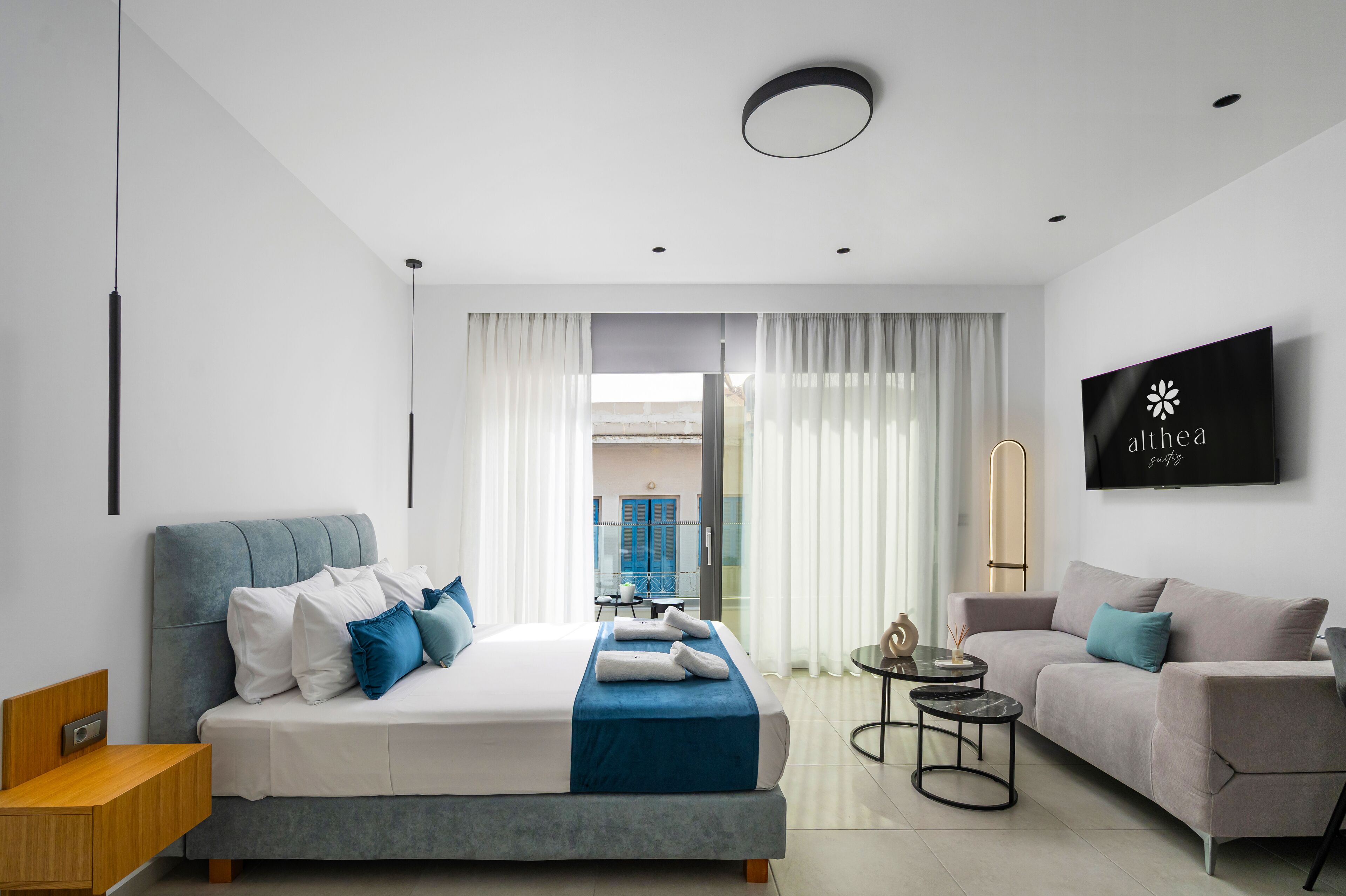 A modern hotel room with a large bed, a sofa, a TV, and a balcony view.
