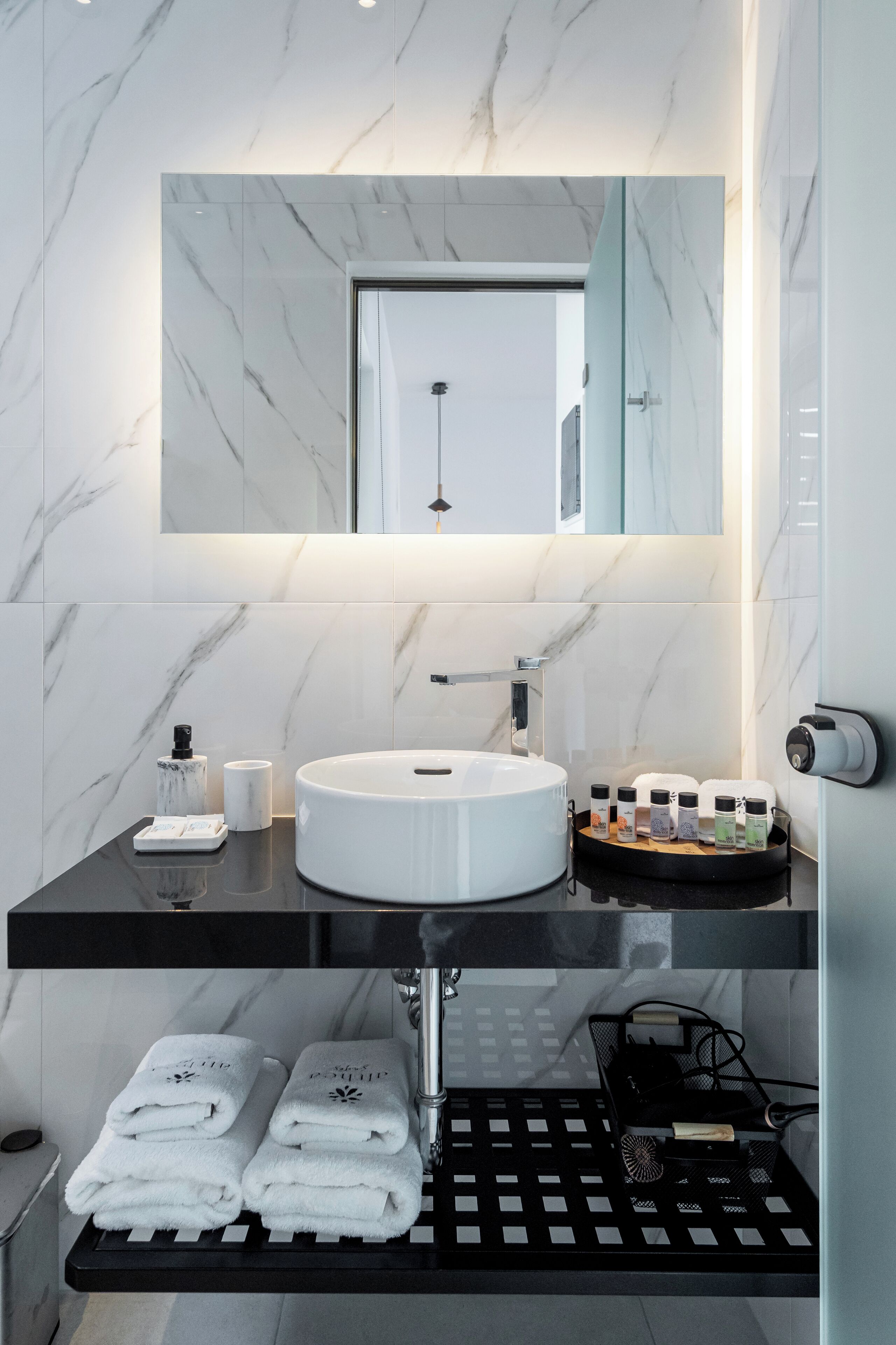 A modern bathroom with a marble backsplash, a white sink, and a mirror above it. There are towels and toiletries on the counter.