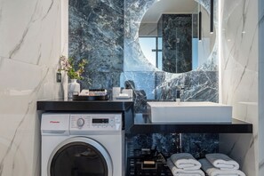 A modern bathroom with a marble backsplash, a washing machine, a sink, and a mirror. - Althea Suites (Sitia)