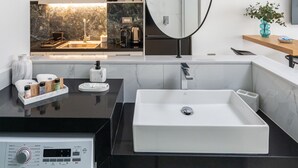 A modern bathroom with a large mirror, a sink, and a washing machine. - Althea Suites (Sitia)