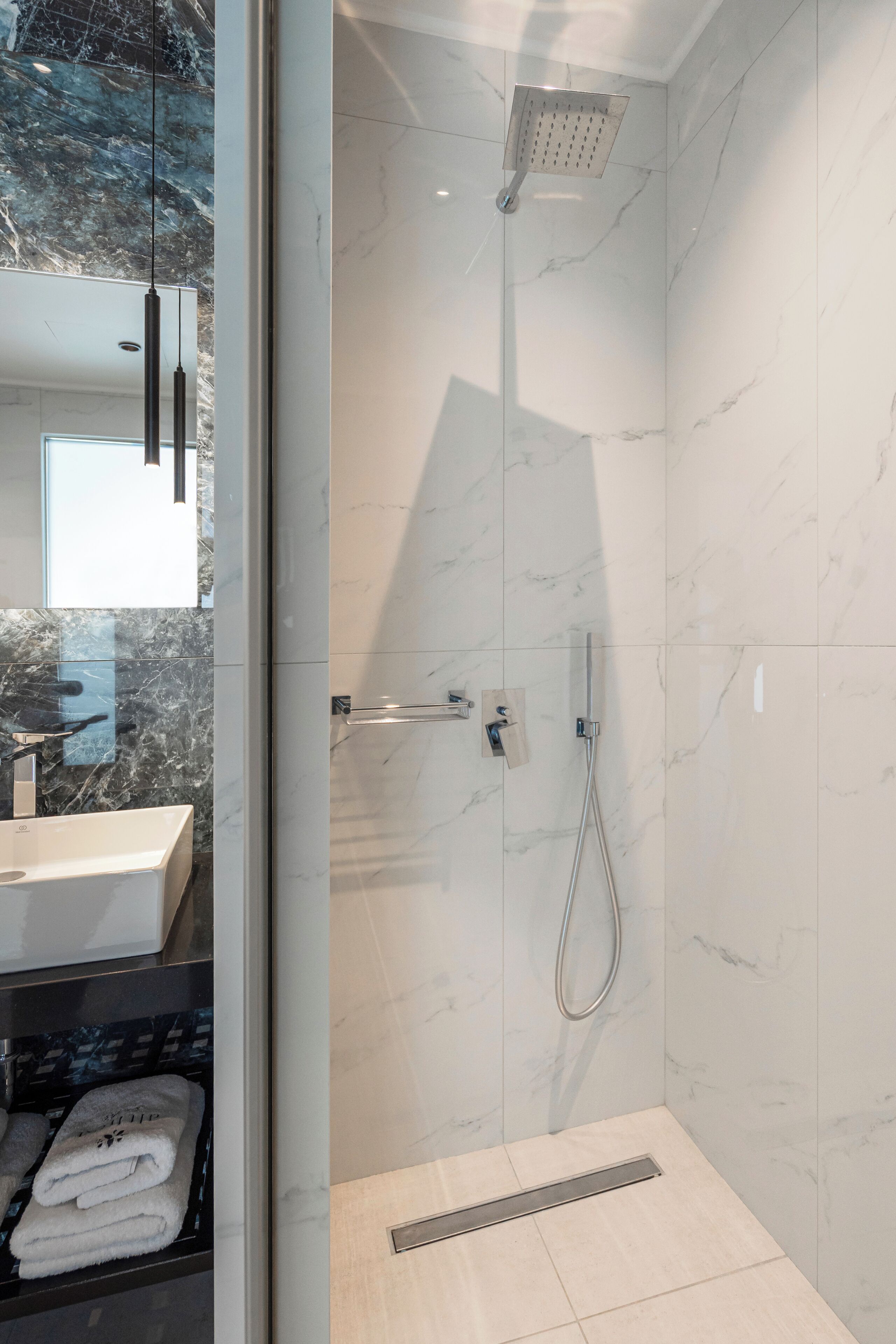 A modern bathroom with a glass-enclosed shower, marble walls, and a visible towel rack.