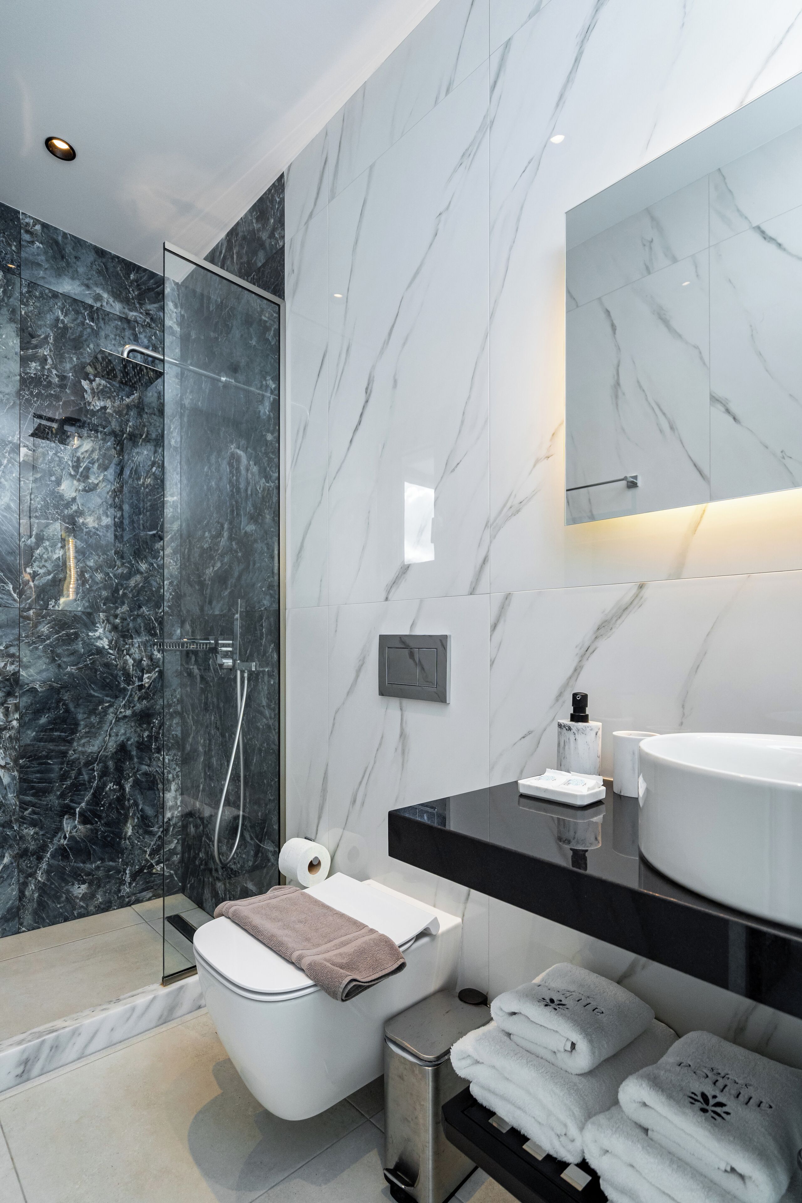 Une salle de bain moderne avec une douche à parois de verre, des toilettes blanches, un meuble-lavabo noir avec un évier blanc et des serviettes soigneusement pliées.