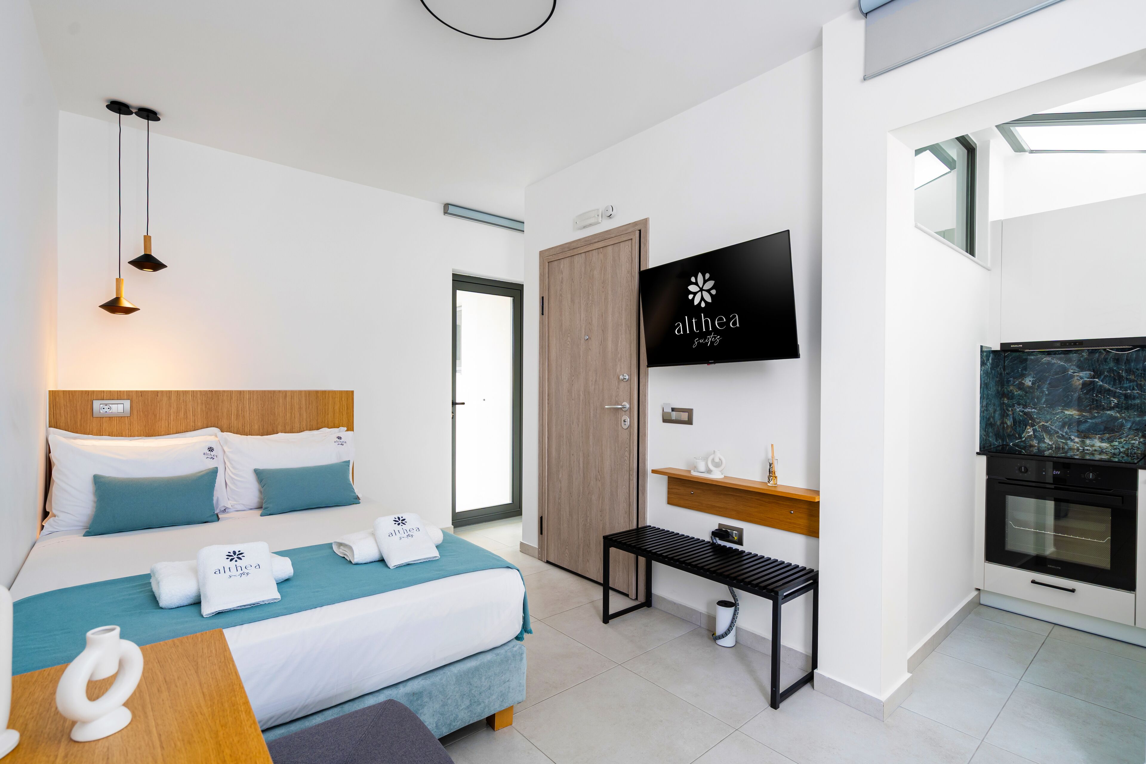 Una habitación de hotel moderna con una cama, televisión, puerta de madera y zona de cocina.